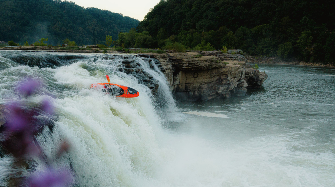 Orange kayak going over raging waterfall